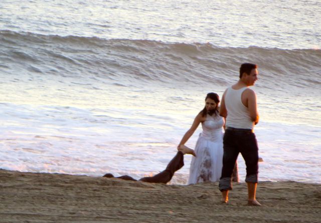 Mexican photographers like to create drama. Both the bride and groom are already wet form the high surf. Here the photographer in the white top jas the groom laying in the beach with the bride pullinj gat his leg.....she is rescuing her husband!!